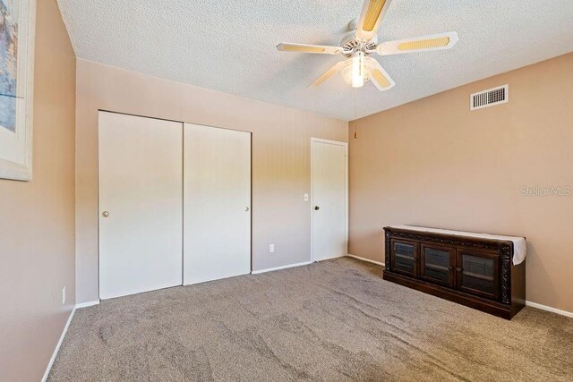 unfurnished bedroom with a textured ceiling, ceiling fan, carpet flooring, and a closet