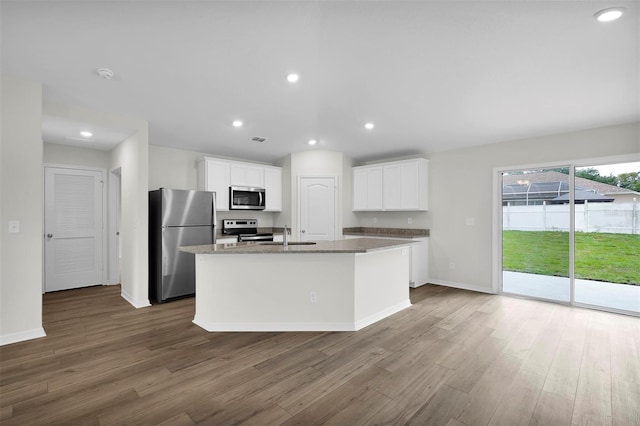 kitchen with wood-type flooring, white cabinets, appliances with stainless steel finishes, stone countertops, and a kitchen island with sink