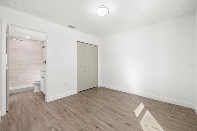 unfurnished bedroom with connected bathroom, light hardwood / wood-style floors, and a closet