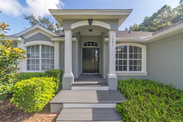 doorway to property with stucco siding and a shingled roof