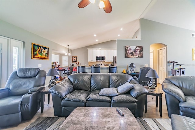 living room featuring light wood finished floors, arched walkways, ceiling fan, and vaulted ceiling