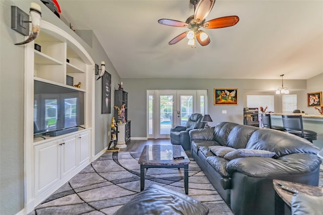 living area with built in shelves, a ceiling fan, wood finished floors, french doors, and baseboards