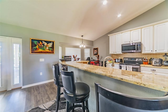 kitchen featuring dark wood-style floors, a sink, stainless steel appliances, vaulted ceiling, and a kitchen bar