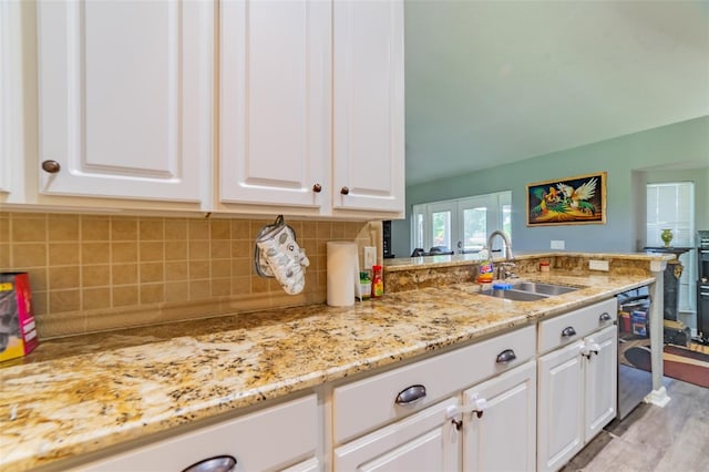 kitchen featuring light stone countertops, a peninsula, a sink, white cabinetry, and backsplash