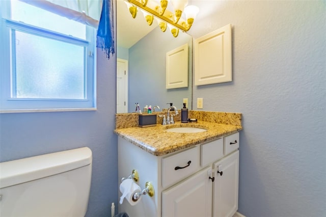 half bathroom featuring vanity, toilet, and a textured wall