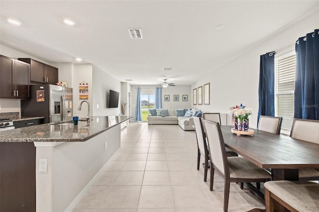 kitchen featuring light tile patterned flooring, dark stone counters, ceiling fan, stainless steel fridge, and sink