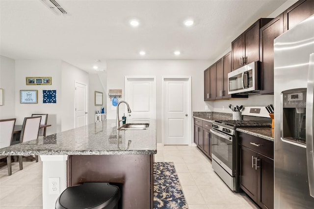 kitchen with a breakfast bar area, light tile patterned floors, an island with sink, stainless steel appliances, and sink