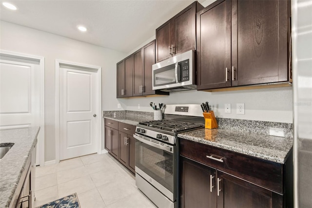 kitchen with appliances with stainless steel finishes, light tile patterned flooring, dark brown cabinets, and light stone countertops