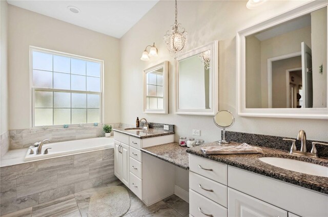 bathroom featuring a notable chandelier, vanity, and a relaxing tiled tub