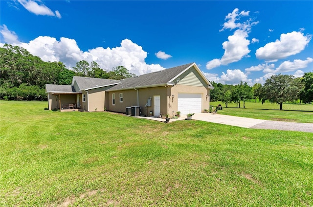 view of side of property with driveway, central AC, an attached garage, a lawn, and stucco siding