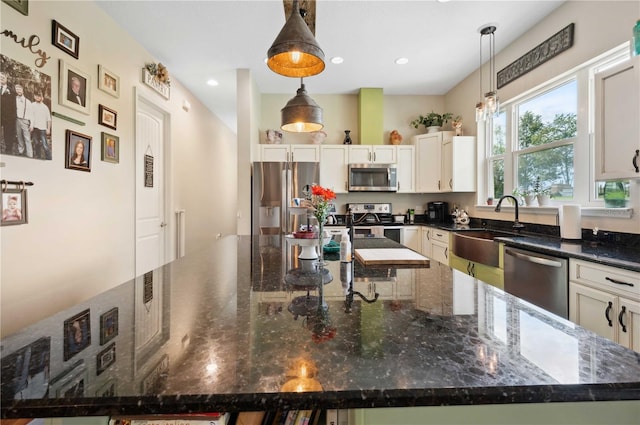 kitchen with stainless steel appliances, a large island, pendant lighting, sink, and dark stone countertops