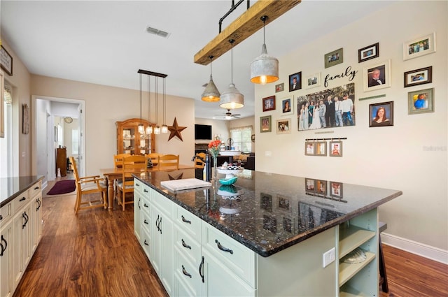 kitchen featuring decorative light fixtures, dark hardwood / wood-style floors, dark stone countertops, ceiling fan, and a center island