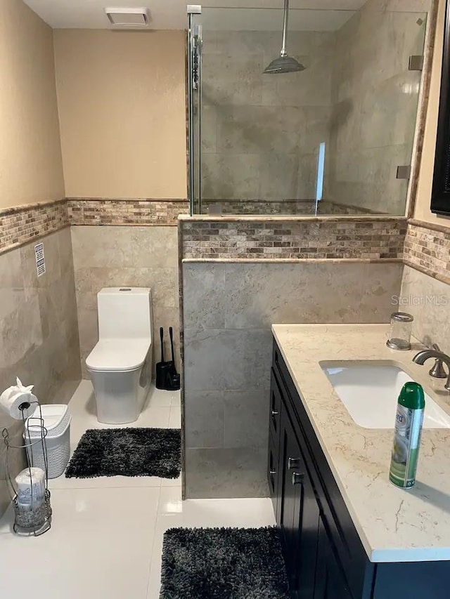 bathroom with vanity, tile patterned floors, tile walls, a tile shower, and toilet