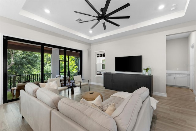 living room featuring a raised ceiling, ceiling fan, and light wood-type flooring