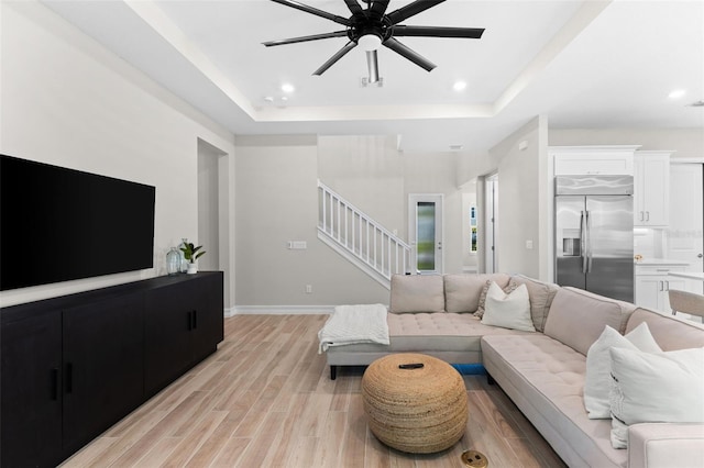 living room with light hardwood / wood-style floors, a raised ceiling, and ceiling fan