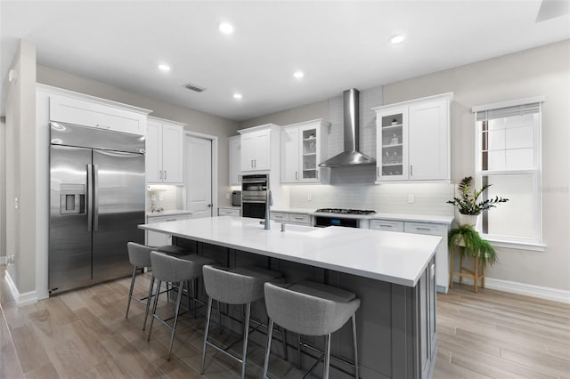 kitchen featuring wall chimney range hood, white cabinets, and appliances with stainless steel finishes