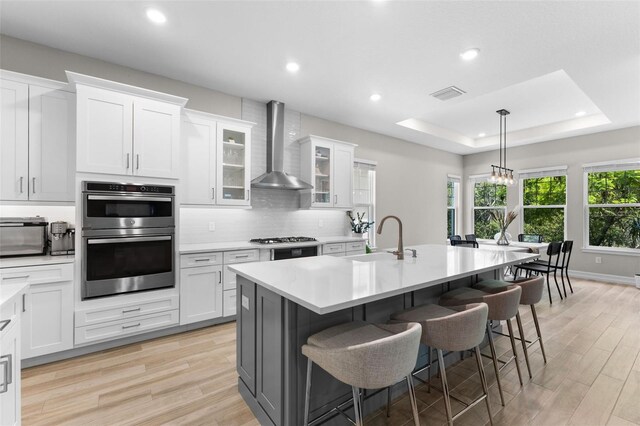 kitchen with a kitchen bar, sink, appliances with stainless steel finishes, wall chimney range hood, and white cabinets