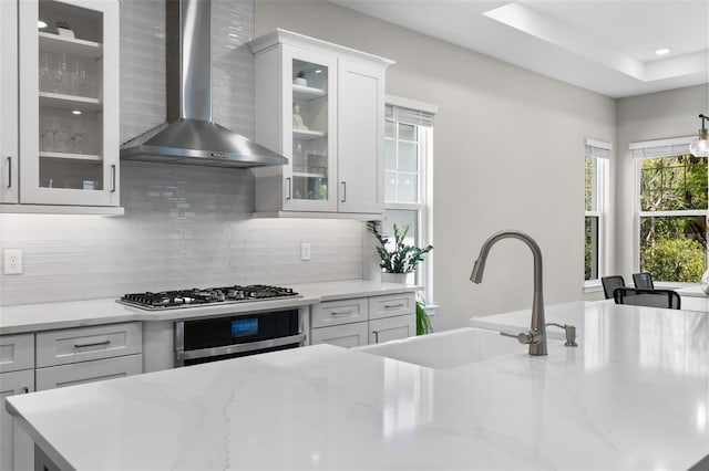 kitchen with sink, appliances with stainless steel finishes, white cabinetry, backsplash, and wall chimney exhaust hood