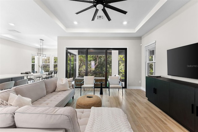 living room with a wealth of natural light, light hardwood / wood-style floors, and a tray ceiling