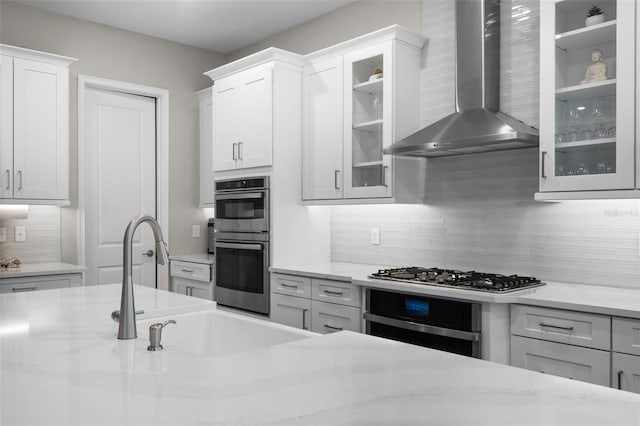 kitchen featuring wall chimney range hood, white cabinetry, stainless steel appliances, light stone counters, and tasteful backsplash