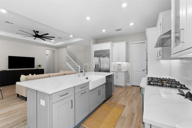 kitchen featuring wall chimney exhaust hood, sink, light wood-type flooring, appliances with stainless steel finishes, and an island with sink