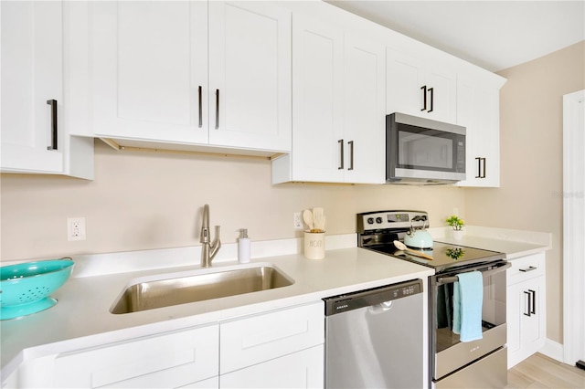 kitchen with appliances with stainless steel finishes, light wood-type flooring, white cabinets, and sink