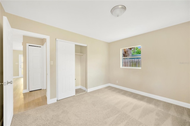 unfurnished bedroom featuring baseboards, a closet, and light colored carpet