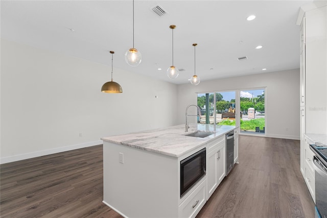 kitchen with white cabinetry, black microwave, sink, pendant lighting, and a center island with sink