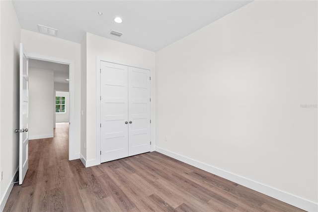 unfurnished bedroom with a closet, visible vents, baseboards, and wood finished floors