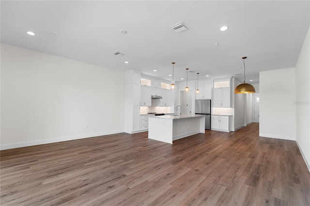 kitchen with white cabinetry, dark wood-type flooring, hanging light fixtures, stainless steel fridge, and a center island with sink