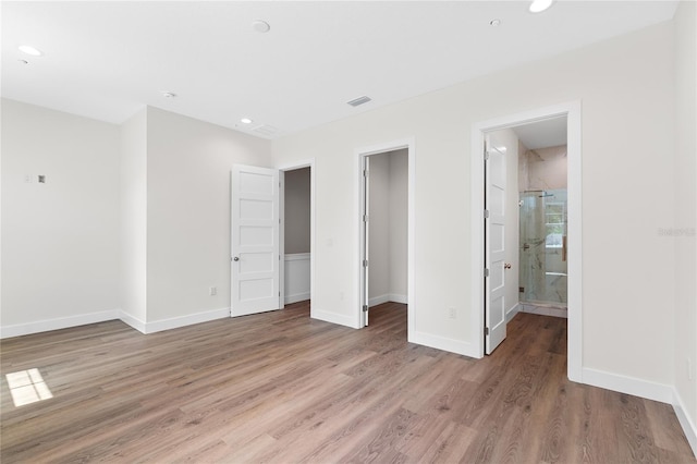 unfurnished bedroom featuring hardwood / wood-style floors, a walk in closet, ensuite bathroom, and a closet