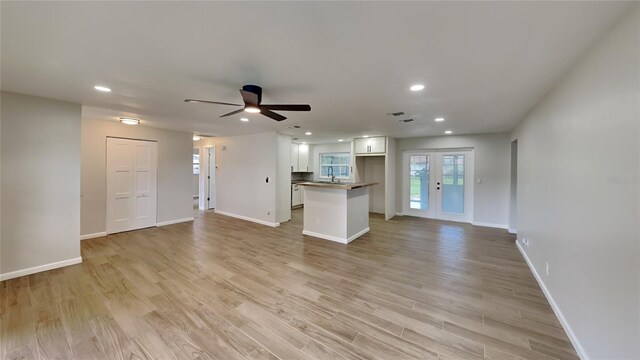 unfurnished living room featuring light hardwood / wood-style floors, french doors, sink, and ceiling fan