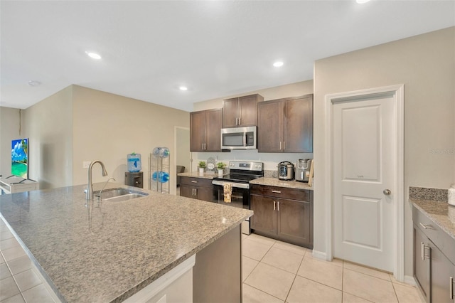 kitchen with light tile patterned flooring, appliances with stainless steel finishes, an island with sink, sink, and dark brown cabinetry