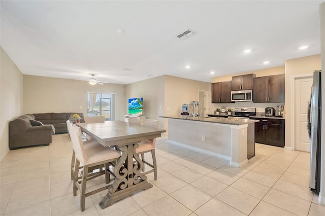 kitchen with stainless steel appliances, light tile patterned flooring, dark brown cabinets, and a center island with sink