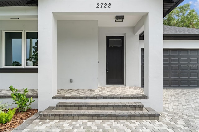 doorway to property with decorative driveway, roof with shingles, and stucco siding