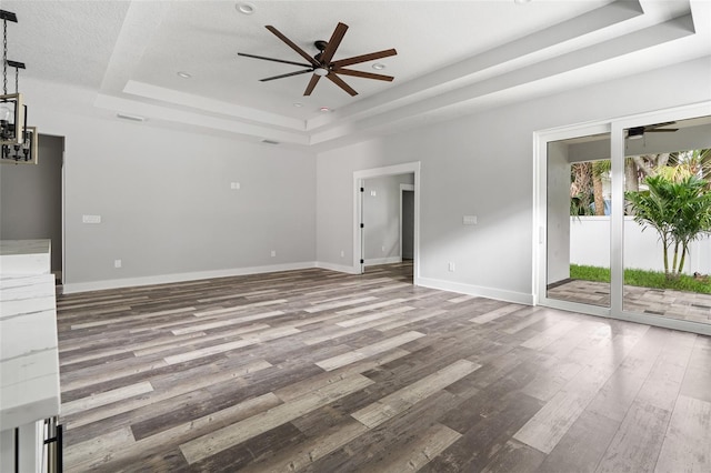 unfurnished living room featuring a ceiling fan, a raised ceiling, baseboards, and wood finished floors