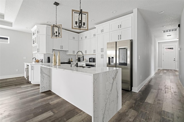 kitchen with stainless steel fridge, white cabinetry, light stone counters, and a sink