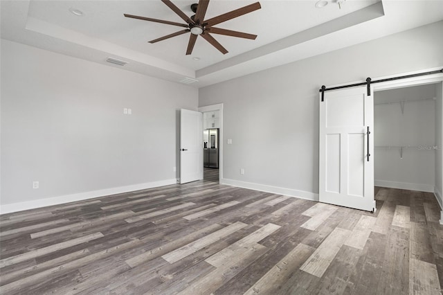 unfurnished bedroom with wood finished floors, a raised ceiling, baseboards, and a barn door