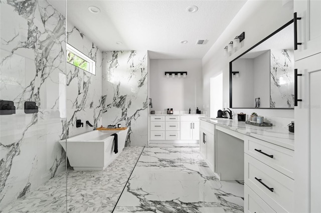 full bath featuring vanity, marble finish floor, a freestanding bath, a textured ceiling, and stone wall