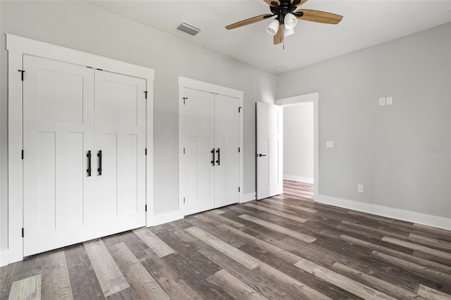 unfurnished bedroom with dark wood-style floors, two closets, visible vents, ceiling fan, and baseboards