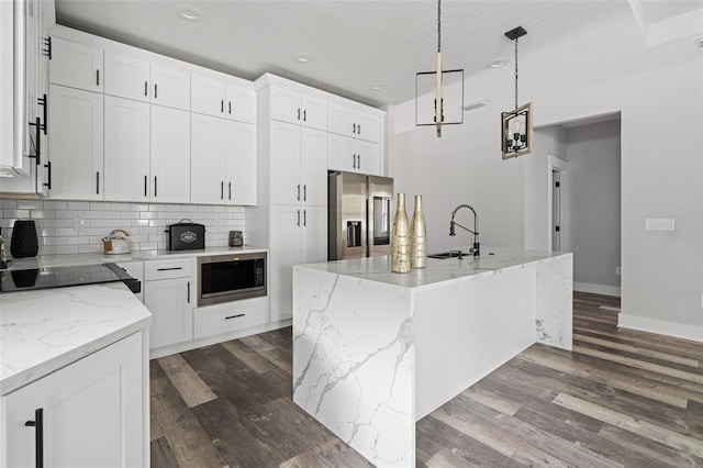 kitchen featuring white cabinets, stainless steel refrigerator with ice dispenser, a kitchen island with sink, and built in microwave