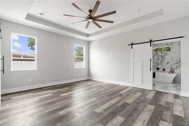 unfurnished bedroom featuring a barn door, a raised ceiling, and baseboards