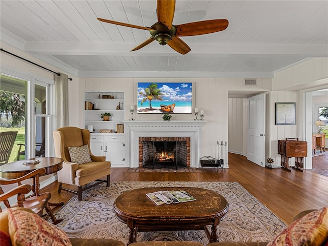 living room with a brick fireplace, built in features, beam ceiling, and dark hardwood / wood-style floors