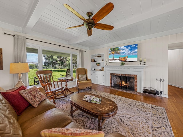 living room featuring ceiling fan, a fireplace, hardwood / wood-style floors, beamed ceiling, and built in features