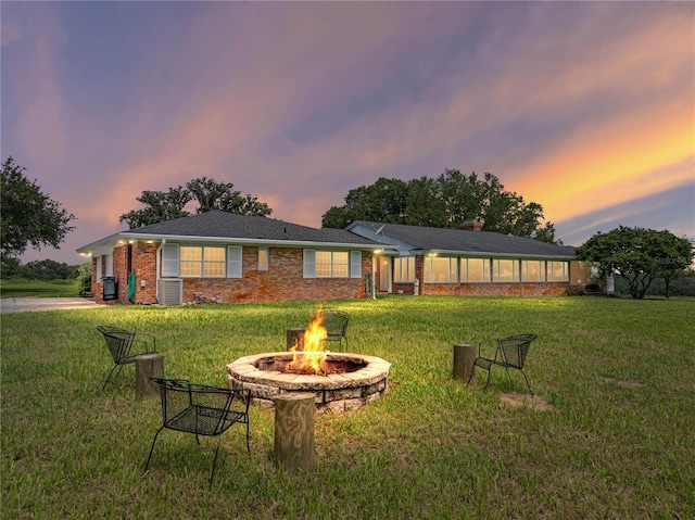 back house at dusk featuring an outdoor fire pit, a yard, and cooling unit