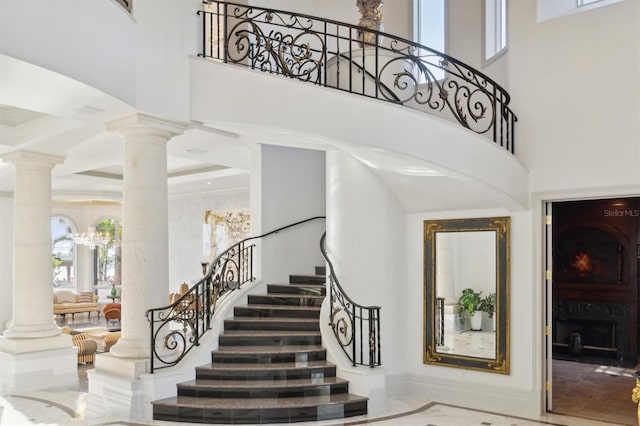 stairs featuring marble finish floor, a notable chandelier, decorative columns, and a high ceiling