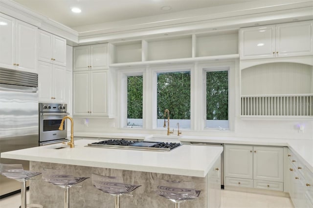 kitchen featuring an island with sink, white cabinets, stainless steel appliances, and light countertops