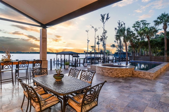 patio terrace at dusk featuring outdoor dining area, a dock, and a water view