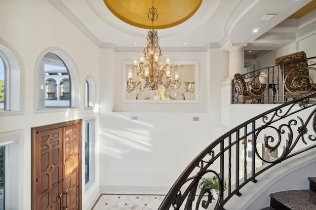 foyer with stairway, an inviting chandelier, visible vents, and crown molding