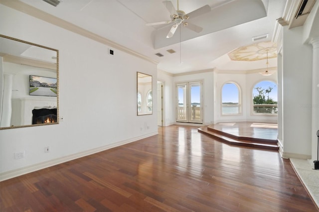 empty room featuring wood finished floors, baseboards, ornamental molding, a raised ceiling, and a glass covered fireplace